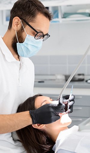 Male dentist in a mask and glasses performing a dental procedure on a patient.