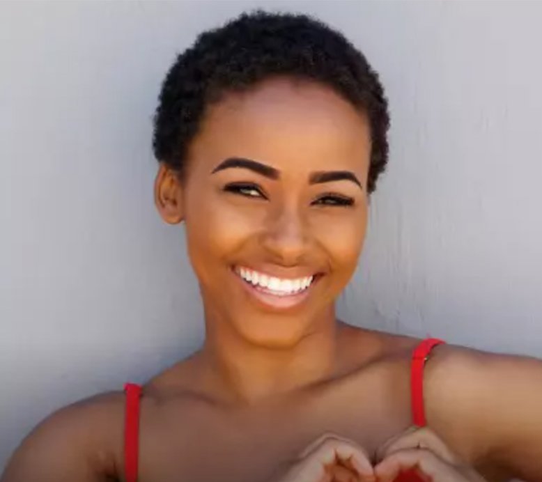 Smiling woman with voluminous curly brown hair and a bright, white smile, looking confidently at the viewer.