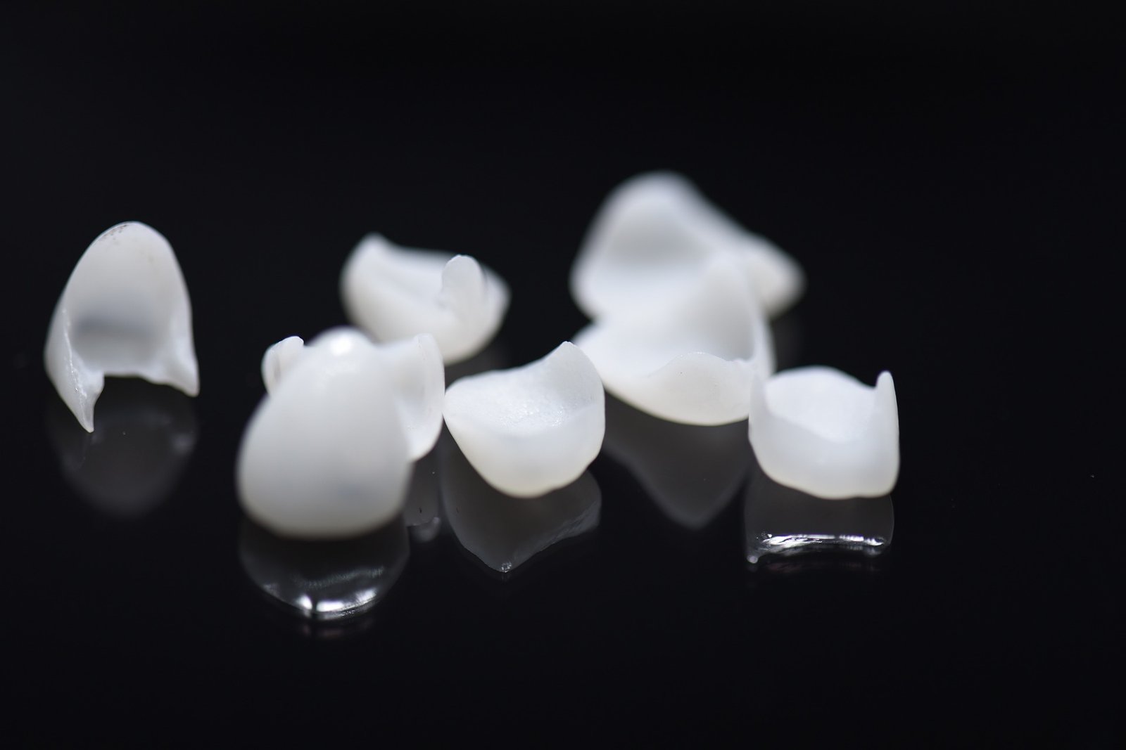 Close-up of several white dental veneers or partial crowns scattered on a black, reflective surface.