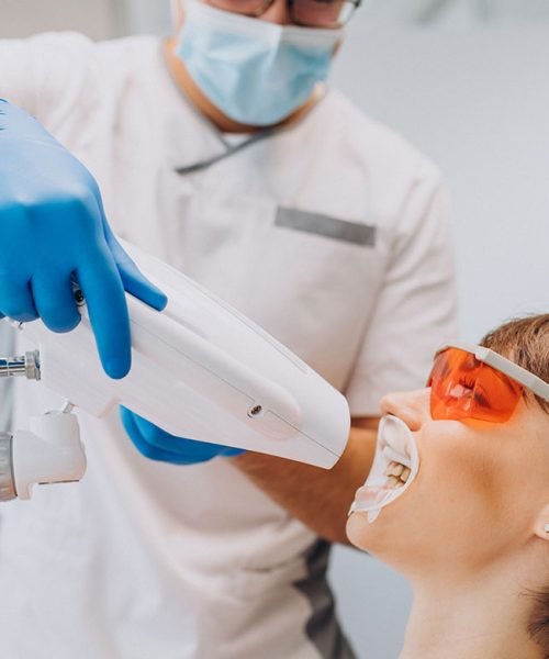 Female patient undergoing professional teeth whitening procedure with protective eyewear