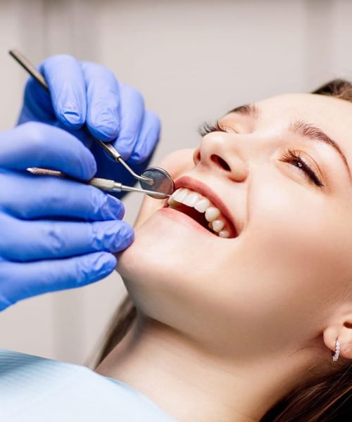 Close-up of a patient's open mouth with a dentist's gloved hands and dental mirror.