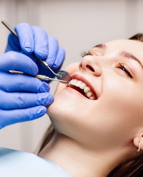 Close-up of a patient's open mouth with a dentist's gloved hands and dental mirror.